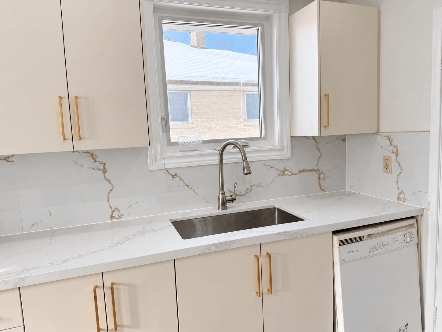White kitchen cabinets, brass handles and a stone-look backsplash